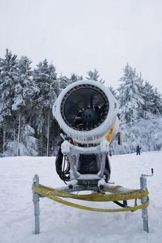 Yellow artificial snow cannon under snow on Wasserkuppe in Rhoen Hesse Germany ski resort on snowy mountain after fresh snow fall. High quality photo