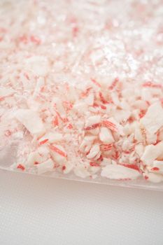 Crushing peppermint candies in a plastic bag with a marble rolling pin on a white cutting board.