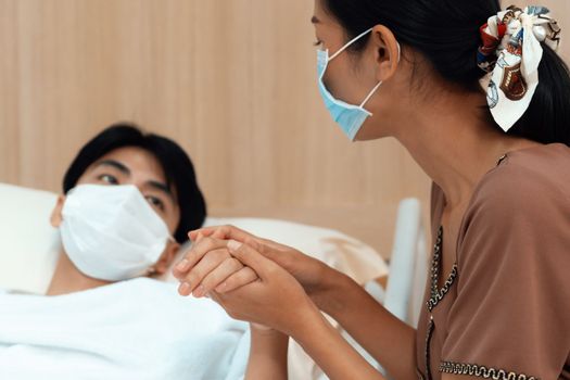 Young patient with attentive visitor and family holding hands in hospital sterile recovery room. The concept of family support for patients receiving hospital care. In-ward medical care and healthcare