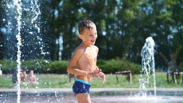 excited boy of seven years having fun between water jets, in fountain, run around, sprinkle, have fun, have fun, on a hot summer day. Summer in the city. Slow motion. High quality photo