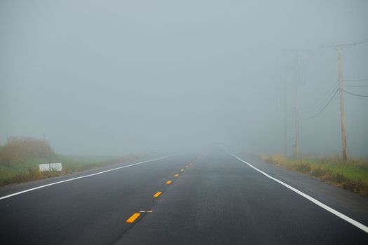 Image of Very foggy road in morning in farmland with row of telephone poles and car in distance