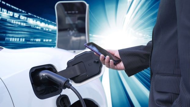 Progressive man charge electric car with power cable plug from charging station with technology background of binary code flying through votex. EV car concept with modern technology.