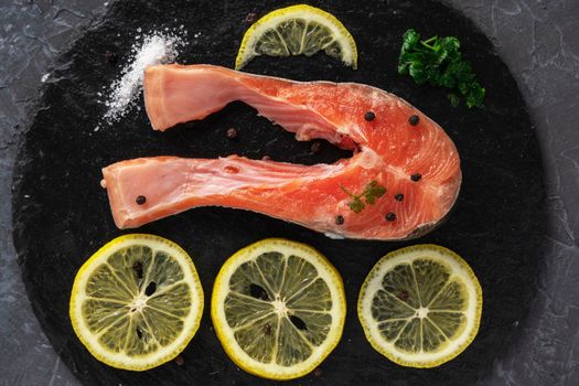 Fish steak with herbs, spices and lemon on a slate black board. Cooking fresh raw trout. Delicious juicy piece of trout for baking for dinner. High quality photo