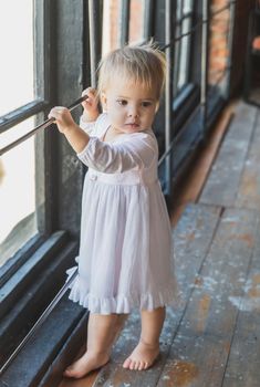 beautiful blonde baby in a nightgown near the window.