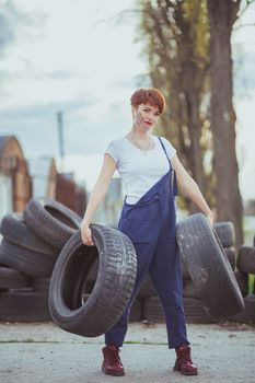 attractive woman mechanic in overalls holding tires.