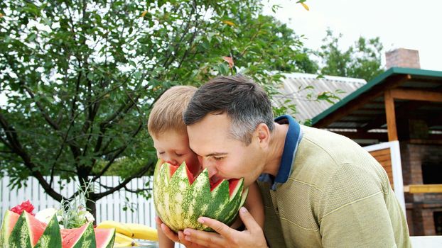 in summer, in the garden, father with a four-year-old son cut a watermelon and eat it, have fun, a boy likes watermelon very much. sweet watermelon for lunch with family. High quality photo