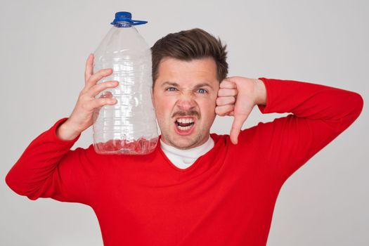 Caucasian man holding empty plastic bottle showing thumb down. Problem with frinking pure water. 