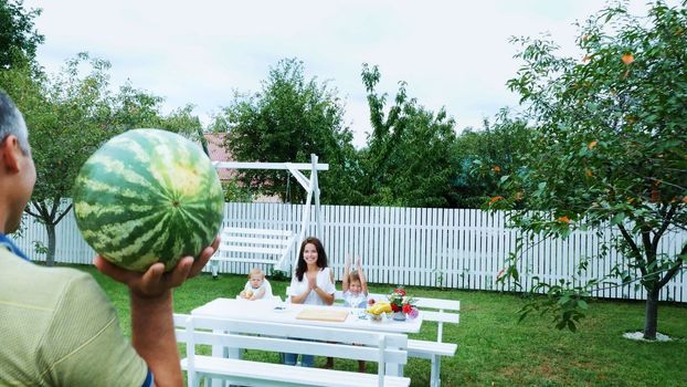 summer, in the garden, Dad bears a large watermelon, is going to treat his family. lunch with the family. The family spends their leisure time together. High quality photo