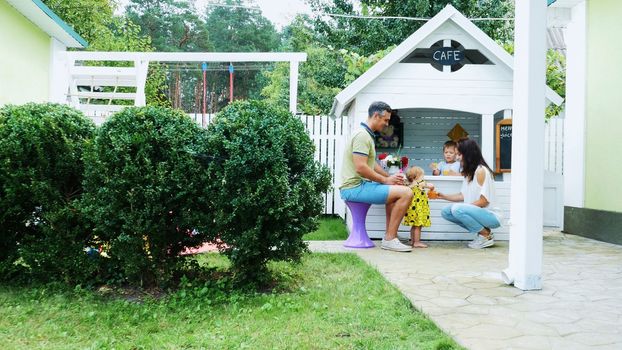 summer, in the garden, parents play with young children, a girl and a boy, in a cafe, in a children's play house, treat children with freshly squeezed fruit juices, drink juices. High quality photo