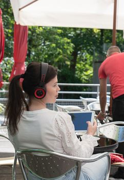 Sad girl listens to music from a tablet at a table in a cafe, High quality photo