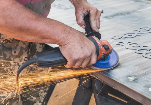 worker scrapes welding welds off a metal workpiece with an angle grinder