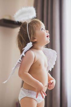 Adorable baby girl with wings and a halo looks up enthusiastically.