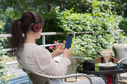 pensive brunette woman in a white blouse, listens to music on headphones at a table in a cafe, High quality photo