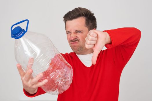 Caucasian man holding empty plastic bottle showing thumb down. Problem with frinking pure water. 