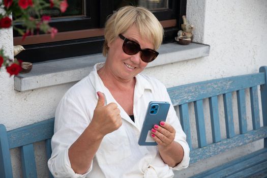 Happy mature middle-aged caucasian woman freelancer using smart phone cellphone for watching webinars video online, surfing social media, working remotely, e-learning at home. High quality photo