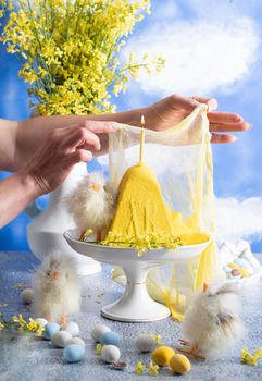 a woman lights a candle on a traditional yellow Slavic Easter curd cake on a blue background against blue sky with white clouds, High quality photo