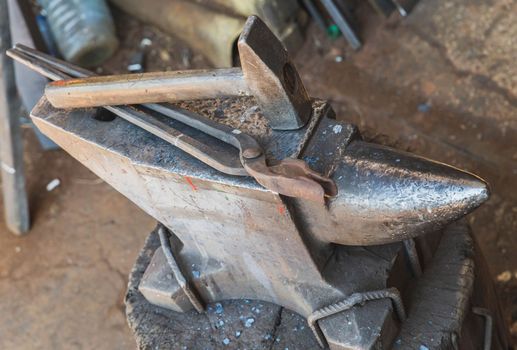 hammer and tongs lie on an anvil in a workshop.