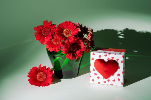 bright red gerberas in a green vase in the rays of multi-colored color still life, heart shaped gift box, Valentine's day concept, High quality photo