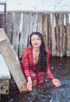 Attractive woman in red dress bathes in the ice-hole in winter.