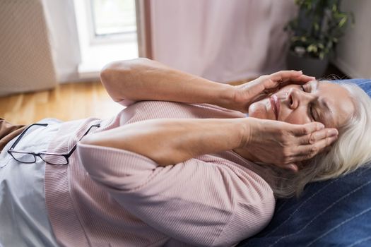 Senior caucasian woman suffering from a headache resting at home on sofa