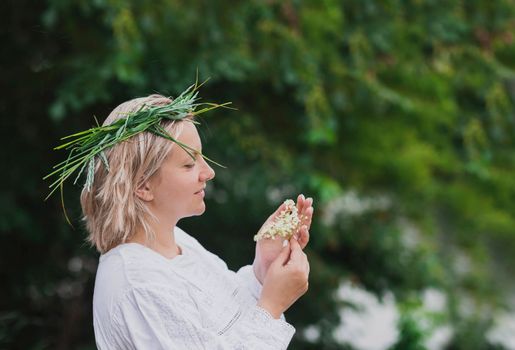 Woman in nightgown with wreath holds elderberry flowers in the forest.