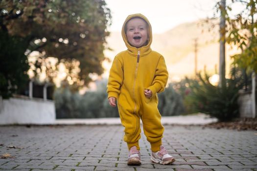 A small child walks outdoor dressed in a yellow jumpsuit. Fresh forest air is good for children's health 