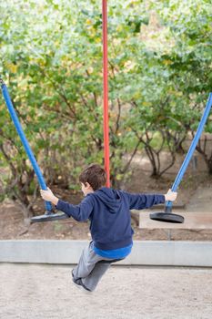 Kid playing with three colourful swing ropes in a park. Rear view.