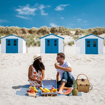 Picnic on the beach Texel Netherlands, couple having a picnic on the coast of Texel with white sand and a colorful withe and blue house in Holland