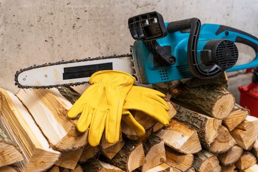 Close-up of a chain saw. electric chain saw and protective leather work gloves on the background of sawn tree trunks. lots of firewood. Firewood harvesting, forest clearing