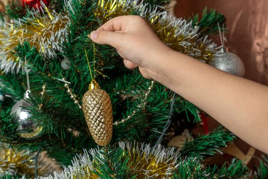 A child dresses up a Christmas tree with toys according to family tradition. Decoration of the apartment for the holiday of Christmas and New Year. Christmas Eve with family. close-up