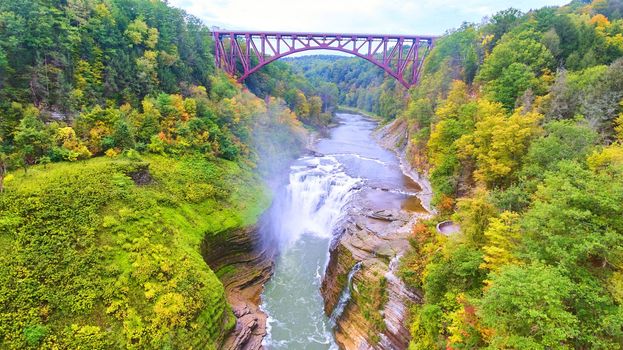 Image of Drone over amazing raging waterfall carving into cliffs with train track bridge above