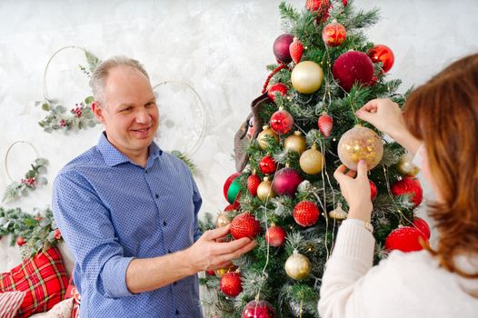 Smiling happy middle age couple decorating christmas tree at home. Happy couple decorating Christmas tree together at home. Happy Family xmas concept