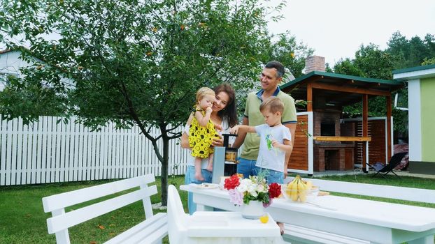 happy beautiful family, mom, dad, four years old son and one-year-old daughter make fresh juice from grapes. In summer, in garden. family spends their leisure time together. High quality photo