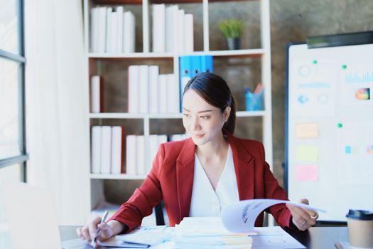 Portrait of a thoughtful Asian businesswoman looking at financial statements and making marketing plans using a computer on her desk.