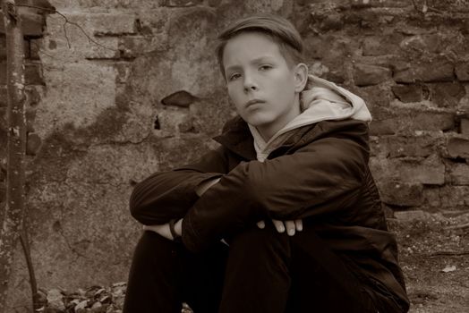 Beautiful boy 13-15 years old sits opposite a brick wall. Black and white portrait of a teenager against an old brick wall.