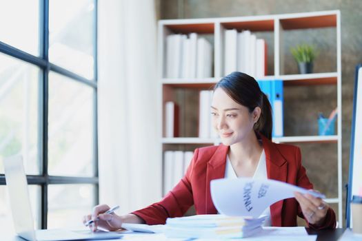 Portrait of a thoughtful Asian businesswoman looking at financial statements and making marketing plans using a computer on her desk.