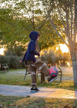 Boy football soccer player doing ball tricks on nature at sunset. Lifestyle outdoors concept