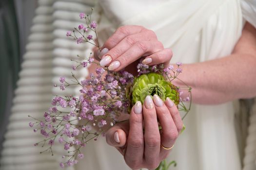 wedding manicure for the bride, a girl in a wedding dress holds a bouquet of ronunculus and pink gypsophila in her hands. High quality photo