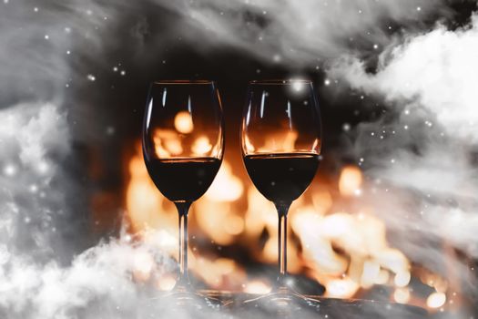 Winter atmosphere and Christmas holiday time, wine glasses in front of fireplace covered with snowy effect on window glass, holidays backgrounds