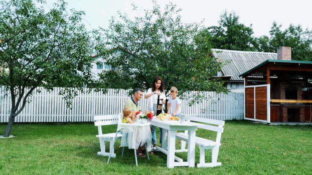 happy beautiful family, mom, dad, four years old son and one-year-old daughter make fresh fruit juice. In summer, in garden. The family spends their leisure time together. High quality photo