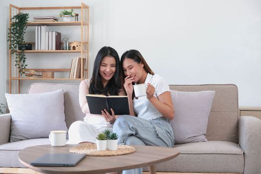 Two female friends reading book while another looking at her smiling playful.