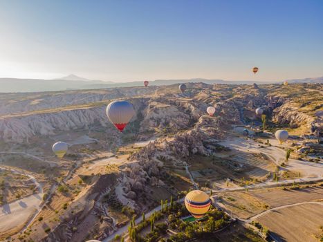 Colorful hot air balloons flying over at fairy chimneys valley in Nevsehir, Goreme, Cappadocia Turkey. Spectacular panoramic drone view of the underground city and ballooning tourism. High quality.