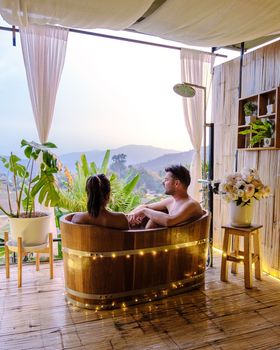 A couple of caucasian men and Asian women in a bathtub in the evening during sunset, a couple in a bathtub.