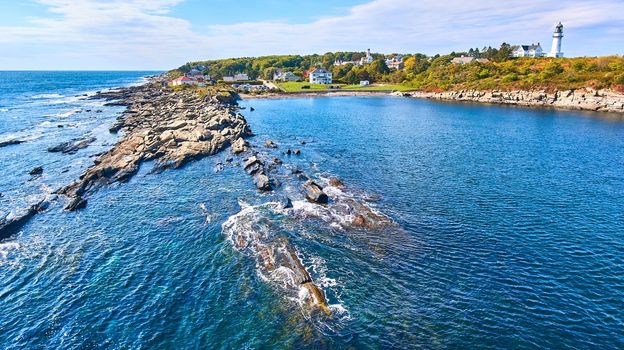 Image of Rocky coastline from over water in Maine with lighthouse in background
