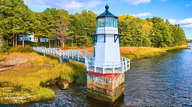 Image of Adorable tiny lighthouse on Maine coast with walkway and fall foliage