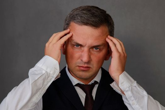 A handsome man touches his temples on his head with his fingers and looks at the camera. 