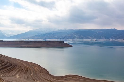 A beautiful reservoir in the mountains. Low water level, drought and beautiful patterns are visible along the banks. A red pleasure boat is standing by the shore