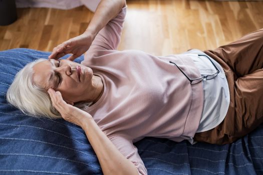 Senior caucasian woman suffering from a headache resting at home on sofa