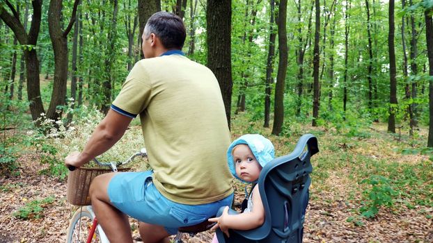 a man with a child riding a bicycle in the forest, in the summer, the child is sitting in a special chair. High quality photo