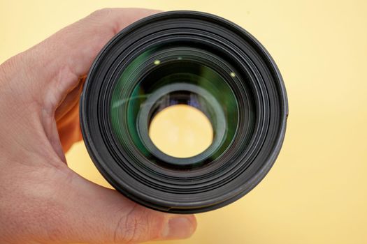 Close-up of a man holding a camera lens in his hand on a yellow background. 